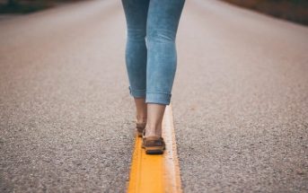 legs and feet of woman walking down middle of road