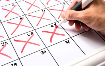 A hand holding a red marker crosses off the 24th day on a calendar. The calendar shows several days already marked with red Xs. The focus is on the hand and the calendar.