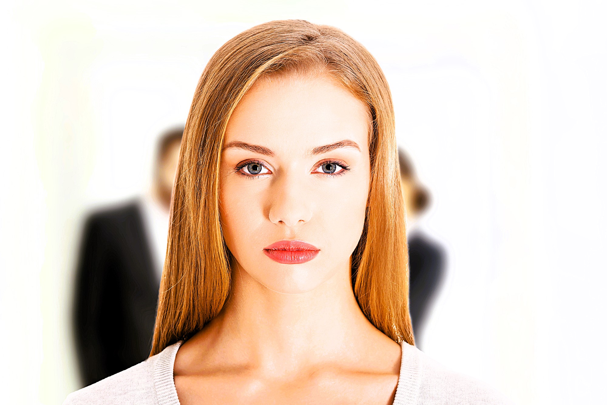 A woman with long blonde hair and red lipstick looks directly at the camera against a white background. Two blurred figures in business attire stand behind her.