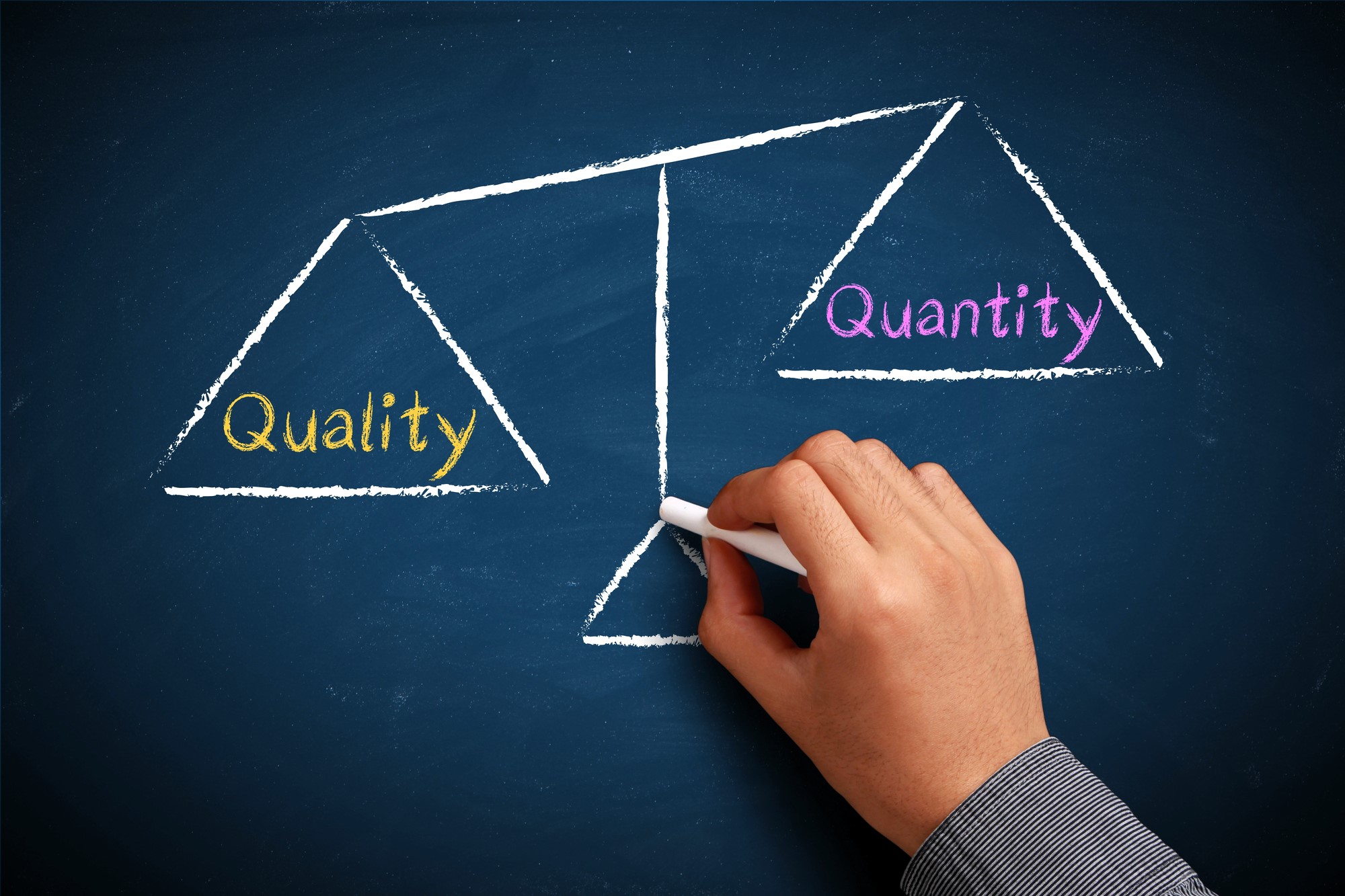 A hand draws a balance scale on a chalkboard. The left side labeled "Quality" is heavier, indicating preference, while the right side labeled "Quantity" is lighter.