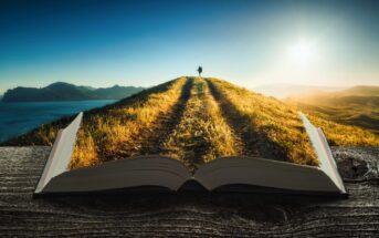 An open book on a wooden surface, with pages transforming into a grassy path leading up a hill. A person stands at the peak, overlooking a landscape under a bright, clear sky. Sunlight casts long shadows along the path.