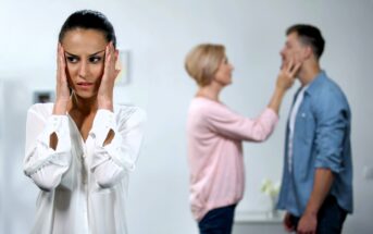 A woman in the foreground looks worried, holding her head with both hands. In the background, a couple is experiencing an argument; a woman is gesturing towards a man's face. The scene suggests tension among the three people.