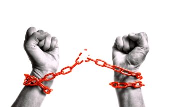 A pair of hands breaking free from red chains against a white background. The fists are clenched, symbolizing liberation or breaking free from constraints.