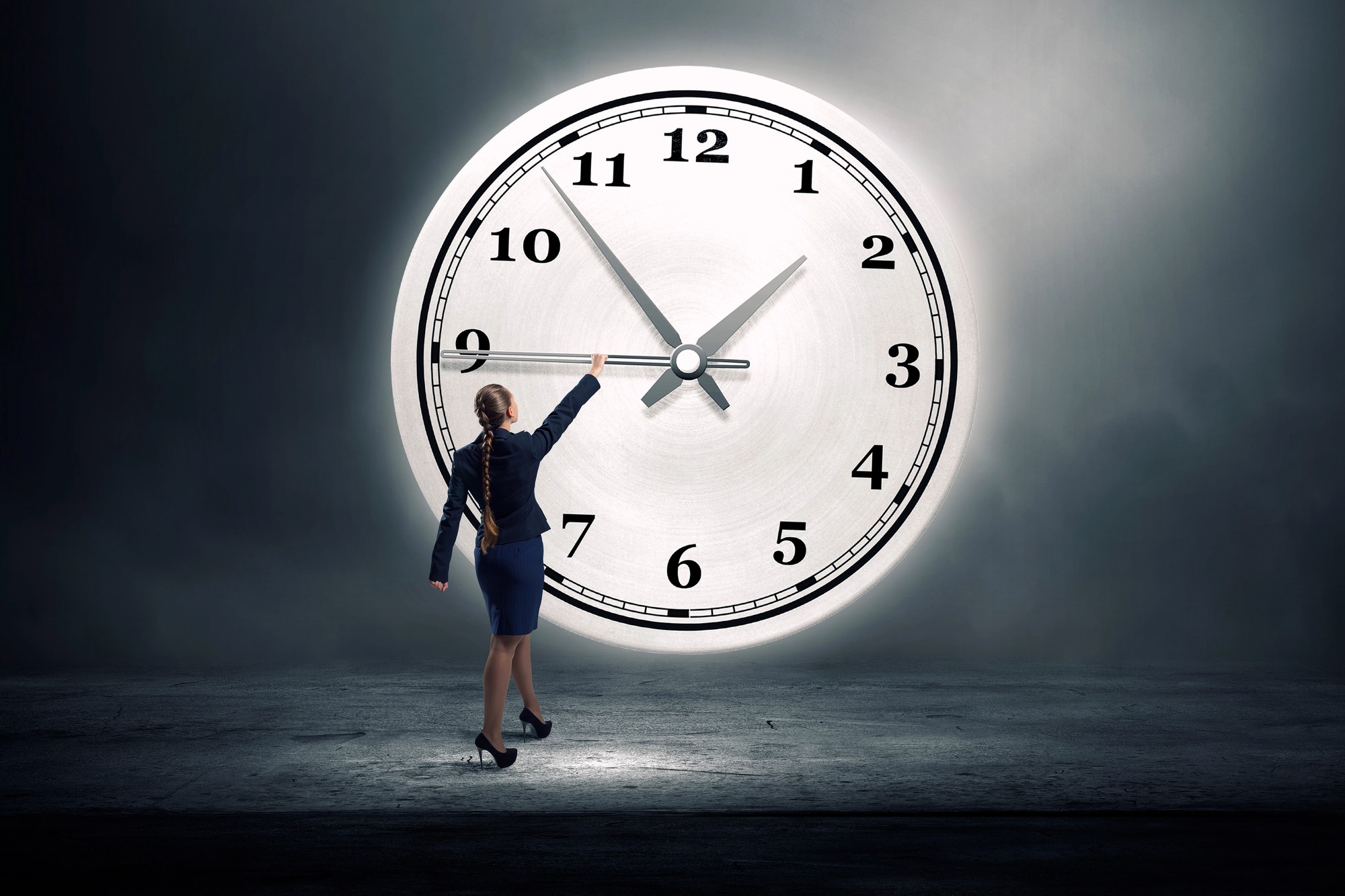 A woman in professional attire stands in front of an oversized clock against a dark background, reaching towards the clock's hands. The clock shows around 10:10. The scene is dramatic and symbolic of time management.