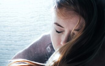 A person with long hair appears submerged in water, eyes closed, and surrounded by light bubbles. Sunlight filters through, casting a serene and ethereal glow across their peaceful expression.