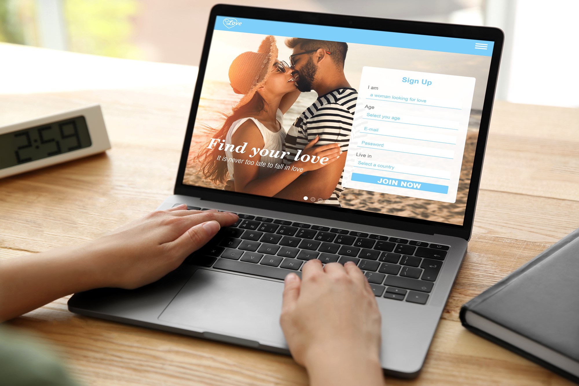 Person using a laptop displaying a dating website. The screen shows a couple embracing under the text "Find your love" and a sign-up form on the right. A clock displays 2:59 in the background.