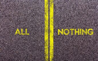 A road with a double yellow line in the middle. The word "ALL" is painted on one side of the line, and "NOTHING" is on the other, both in yellow. The texture of the asphalt is visible.