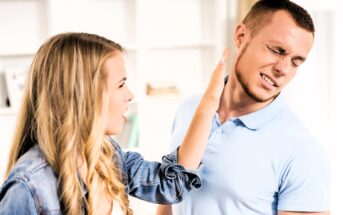 A woman with long blonde hair appears to be in the middle of slapping a man who is wincing in pain. Both are dressed in casual clothing, and the background shows a blurred indoor setting.