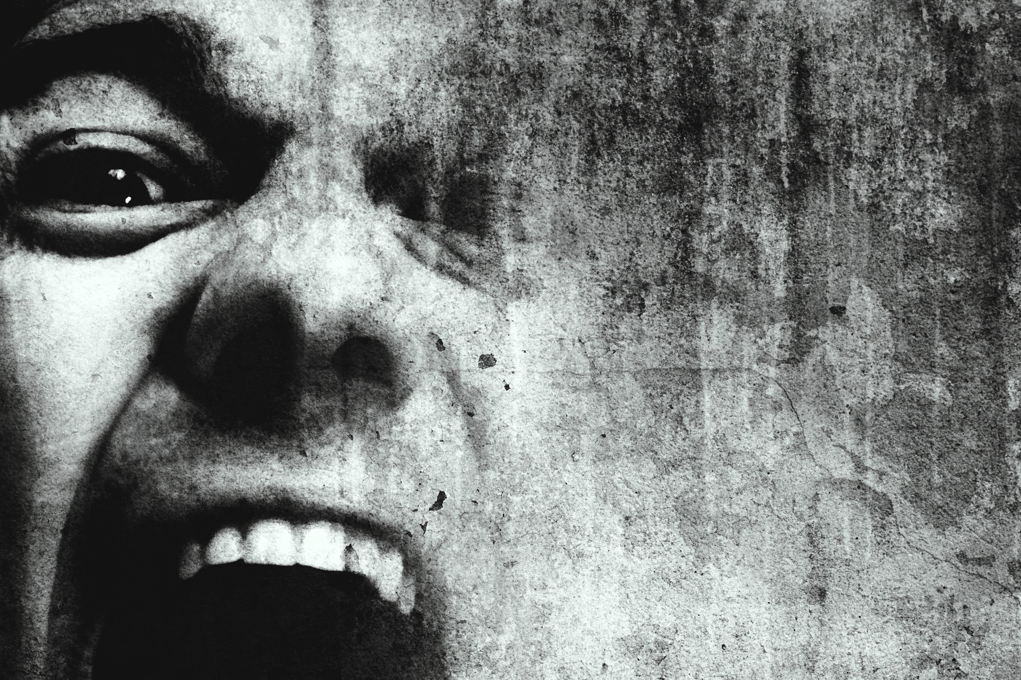 A close-up of a face in black and white, showing one eye and an open mouth with visible teeth, giving an expression of intense emotion. The image has a textured, gritty overlay, adding to the dramatic effect.