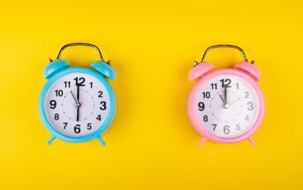 Two alarm clocks on a yellow background: one blue on the left showing 10:09 and one pink on the right showing 3:54. Both clocks have classic twin bell designs with metal handles.