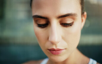 A close-up image of a person with an expression of calm contemplation, looking downwards. The background is blurred, accentuating the focus on the person's face. The person has a serene and peaceful demeanor.