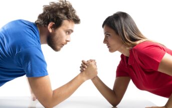 a man in a blue t-shirt on the left arm wrestling with a woman in a red t-shirt on the right