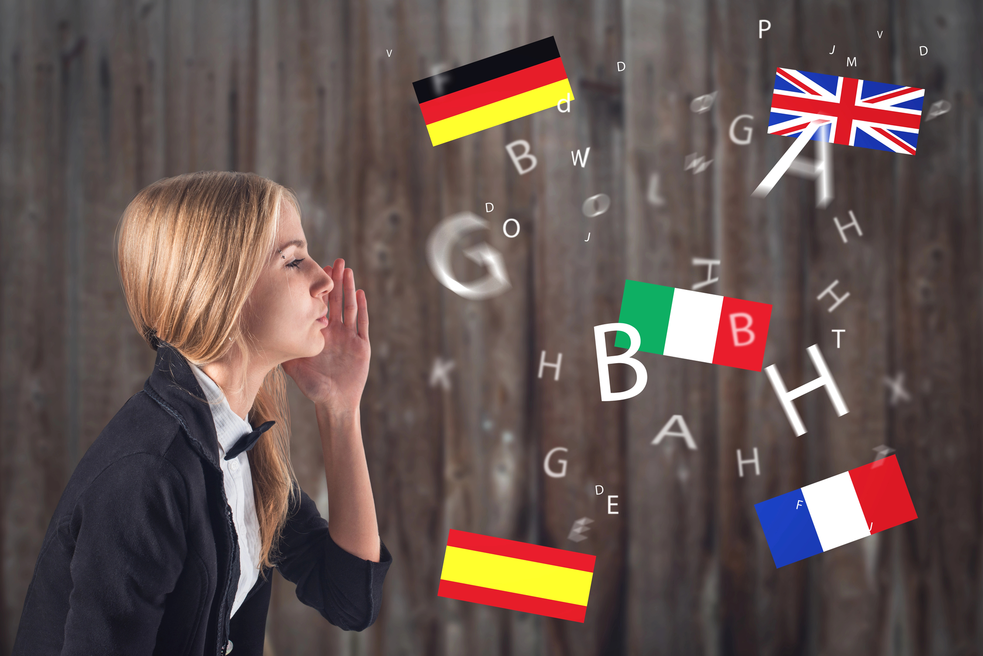 A woman is leaning forward with her hand near her lips as if whispering or speaking. Letters and country flags, including those of Germany, the UK, Italy, Spain, and France, are scattered in the air against a wooden background.