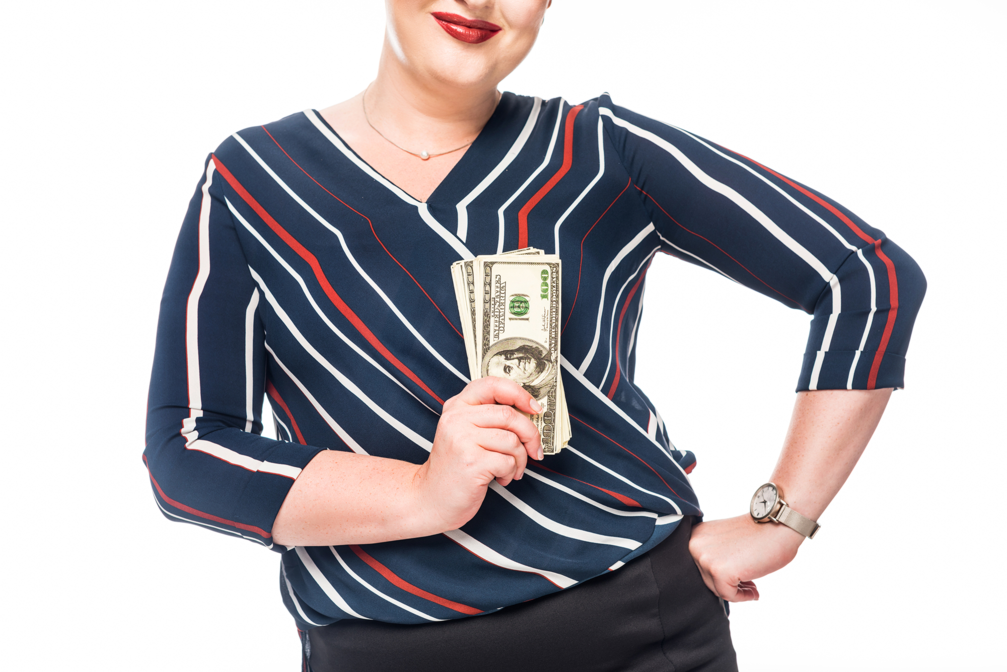 A person with short hair, wearing a striped blouse and a watch, holds a fan of US 100-dollar bills. They have a smile and are posing against a white background.