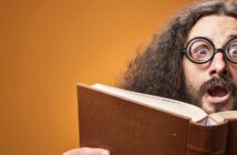 quirky man with circular geek glasses looking interestingly at a book