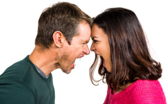 A man and a woman are facing each other with their foreheads touching, both yelling aggressively. The man is wearing a dark green shirt, and the woman is wearing a bright pink sweater. The background is plain white.