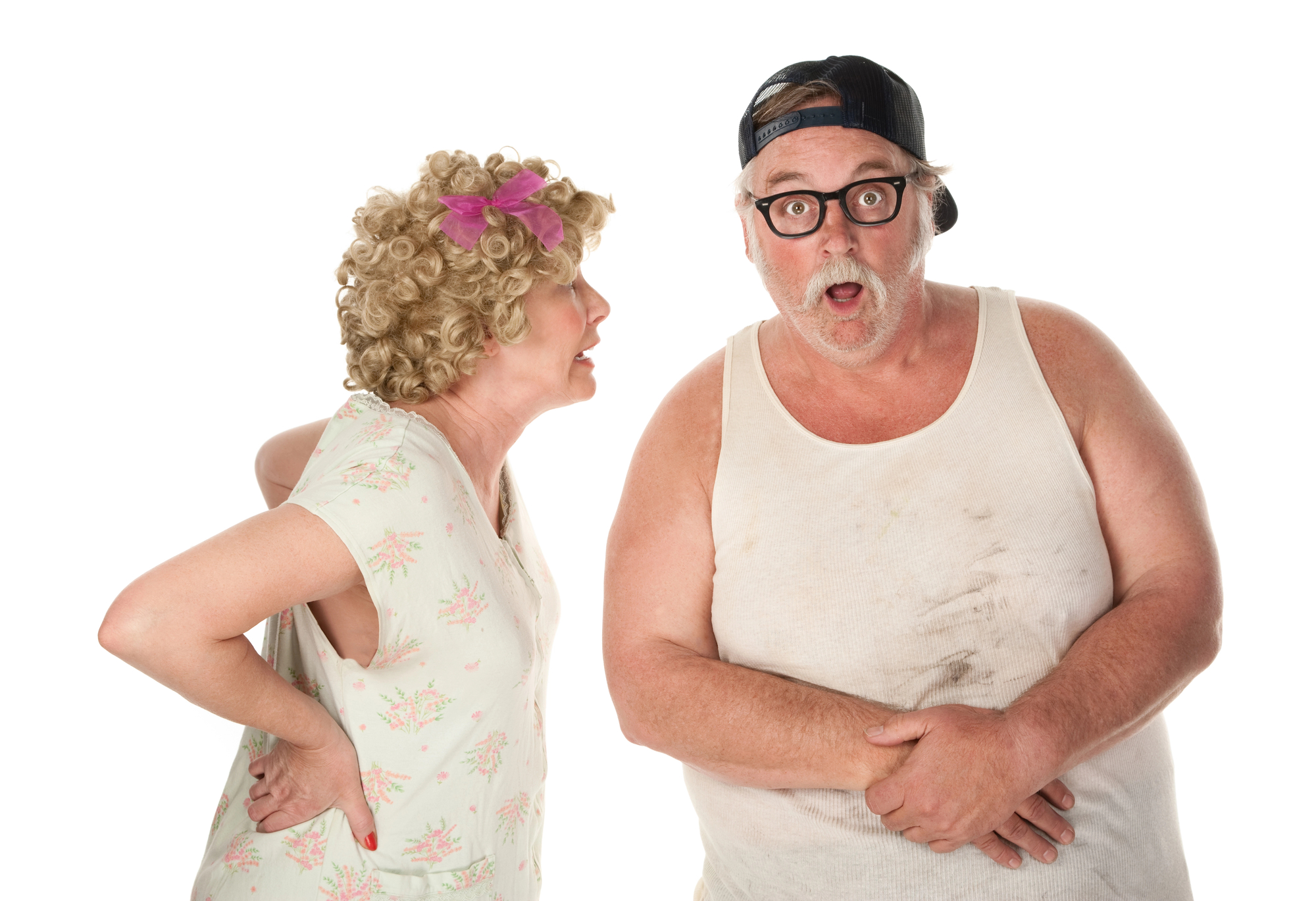 An elderly woman with curly hair and a pink bow, wearing a floral dress, appears to be scolding a bearded man in a dirty tank top, glasses, and a backwards cap. The man looks surprised and holds his hands near his stomach. They stand against a white background.