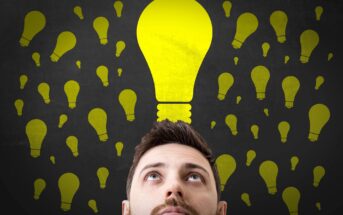 A man looking up thoughtfully with numerous yellow lightbulbs of various sizes floating above his head against a dark background, suggesting the concept of ideas or creativity.