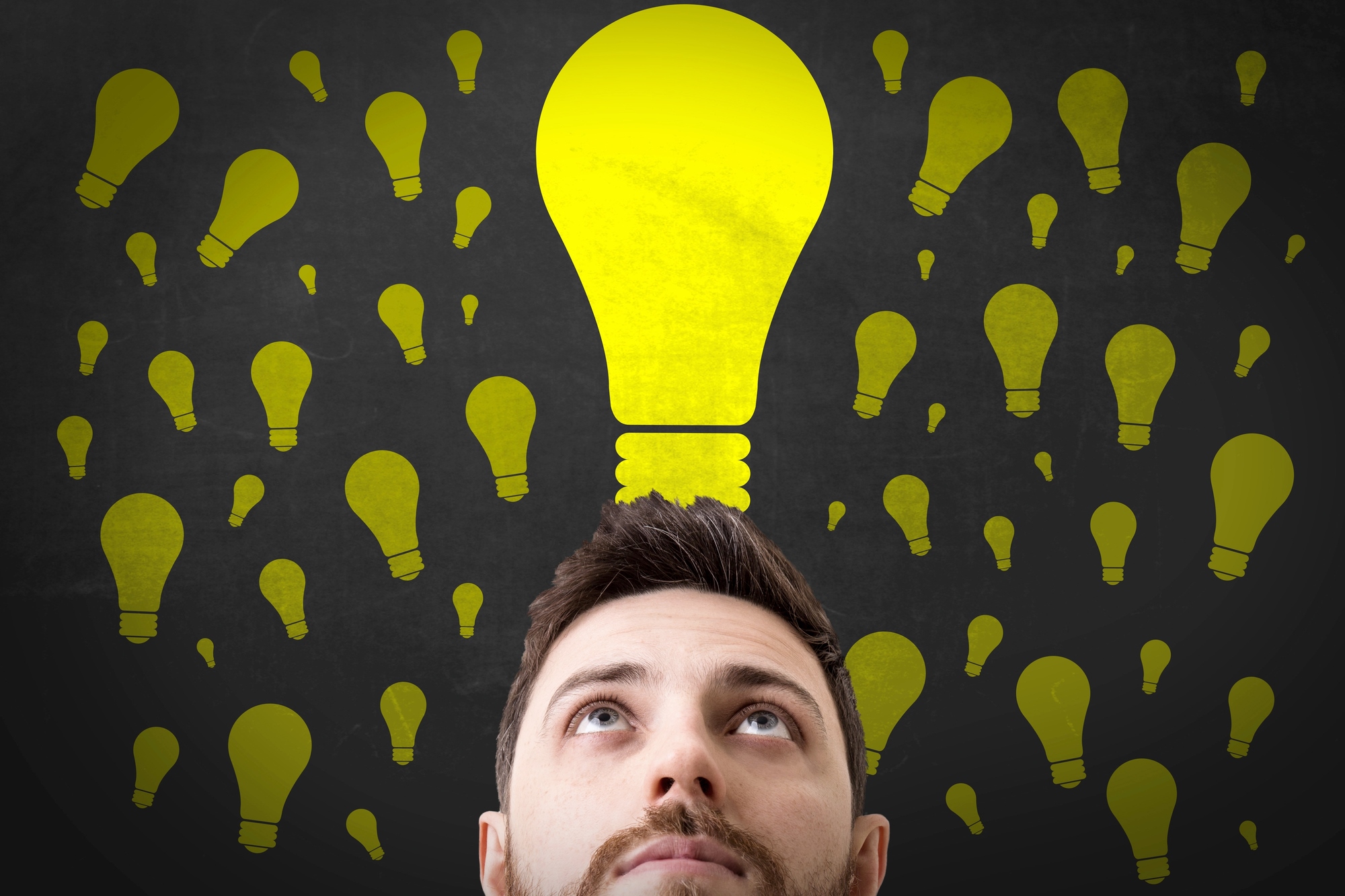 A man looking up thoughtfully with numerous yellow lightbulbs of various sizes floating above his head against a dark background, suggesting the concept of ideas or creativity.