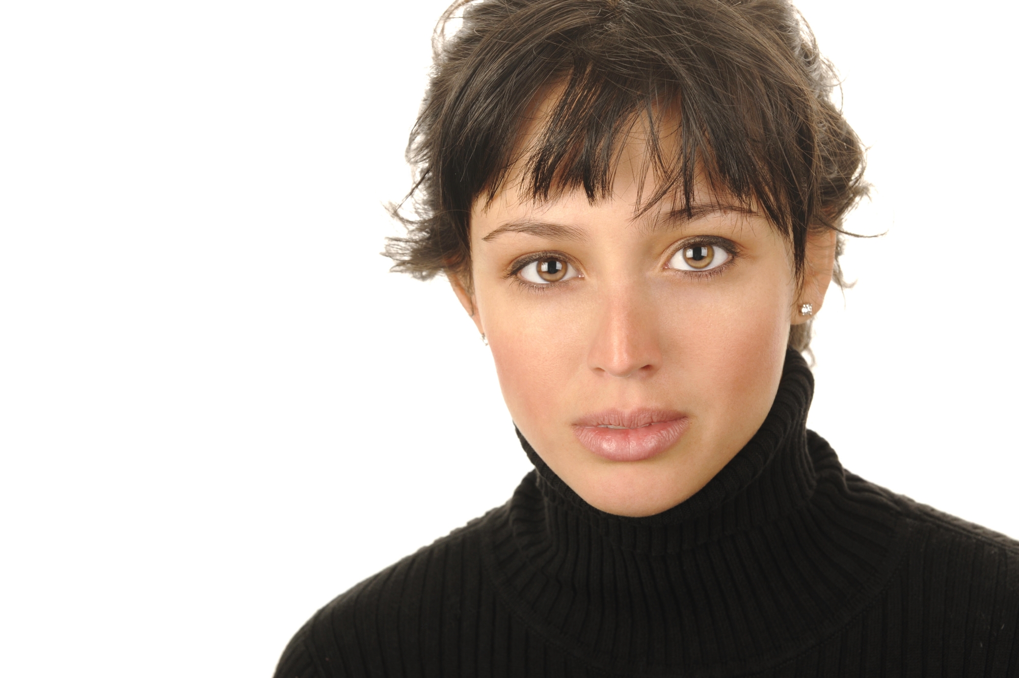 A woman with short, dark hair and bangs is wearing a black turtleneck sweater. She is looking directly at the camera with a neutral expression. The background is plain white. She also has small stud earrings.