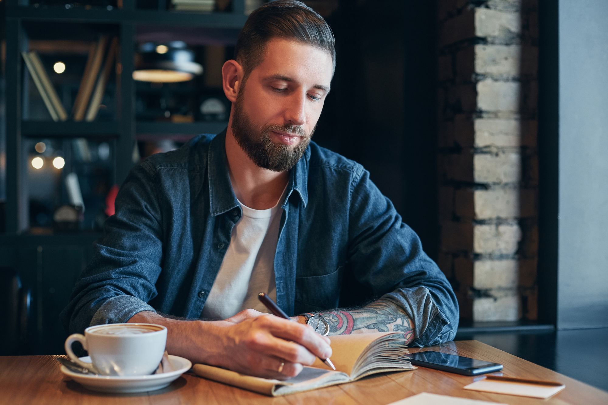 Man hand with pen writing on notebook or journal on a wooden table.