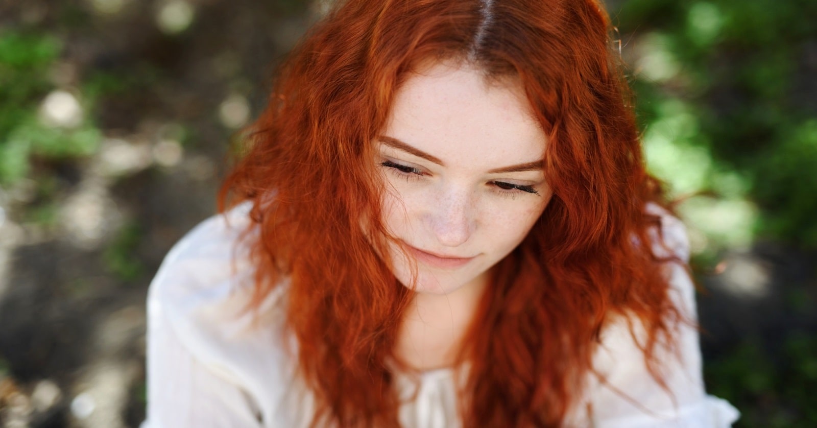 young red head woman wearing a white blouse looking down in a manner that suggests a lack of self-respect.