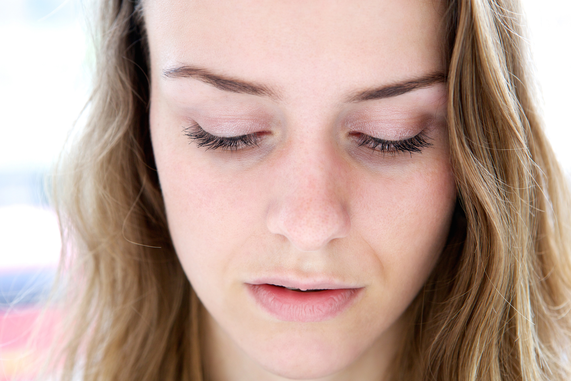 Close-up shot of a woman with light skin and wavy brown hair, looking down with closed eyes, displaying long eyelashes, and a neutral facial expression.