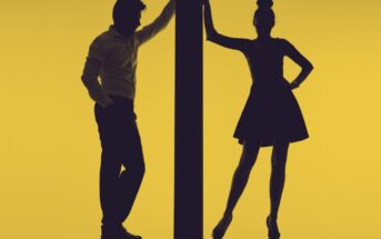 Silhouette of a man and a woman standing on either side of a vertical beam against a yellow background. The man is leaning with one arm on the beam, and the woman is standing with one hand on the beam and the other hand on her hip.