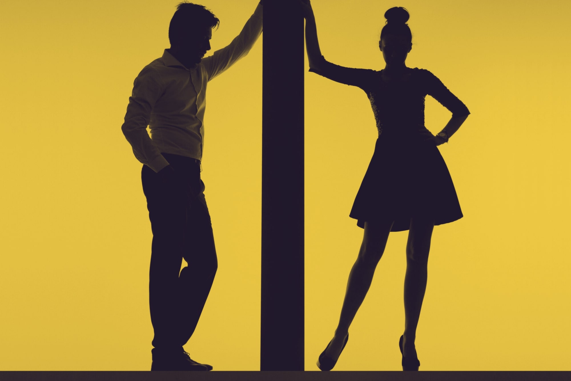 Silhouette of a man and a woman standing on either side of a vertical beam against a yellow background. The man is leaning with one arm on the beam, and the woman is standing with one hand on the beam and the other hand on her hip.