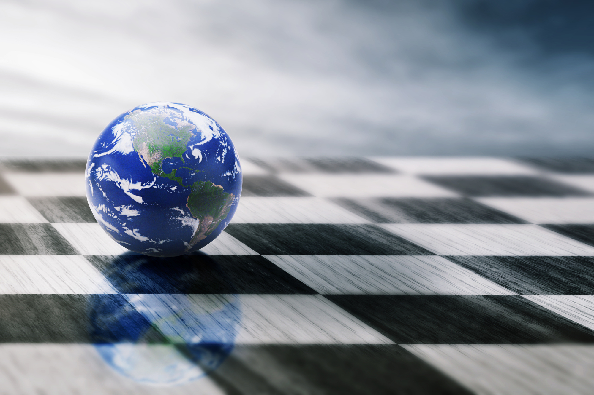 A small globe depicting Earth sits on a black-and-white checkered surface. The background is a gradient of light to dark, creating a dramatic contrast. The globe's reflection is faintly visible on the checkered floor.