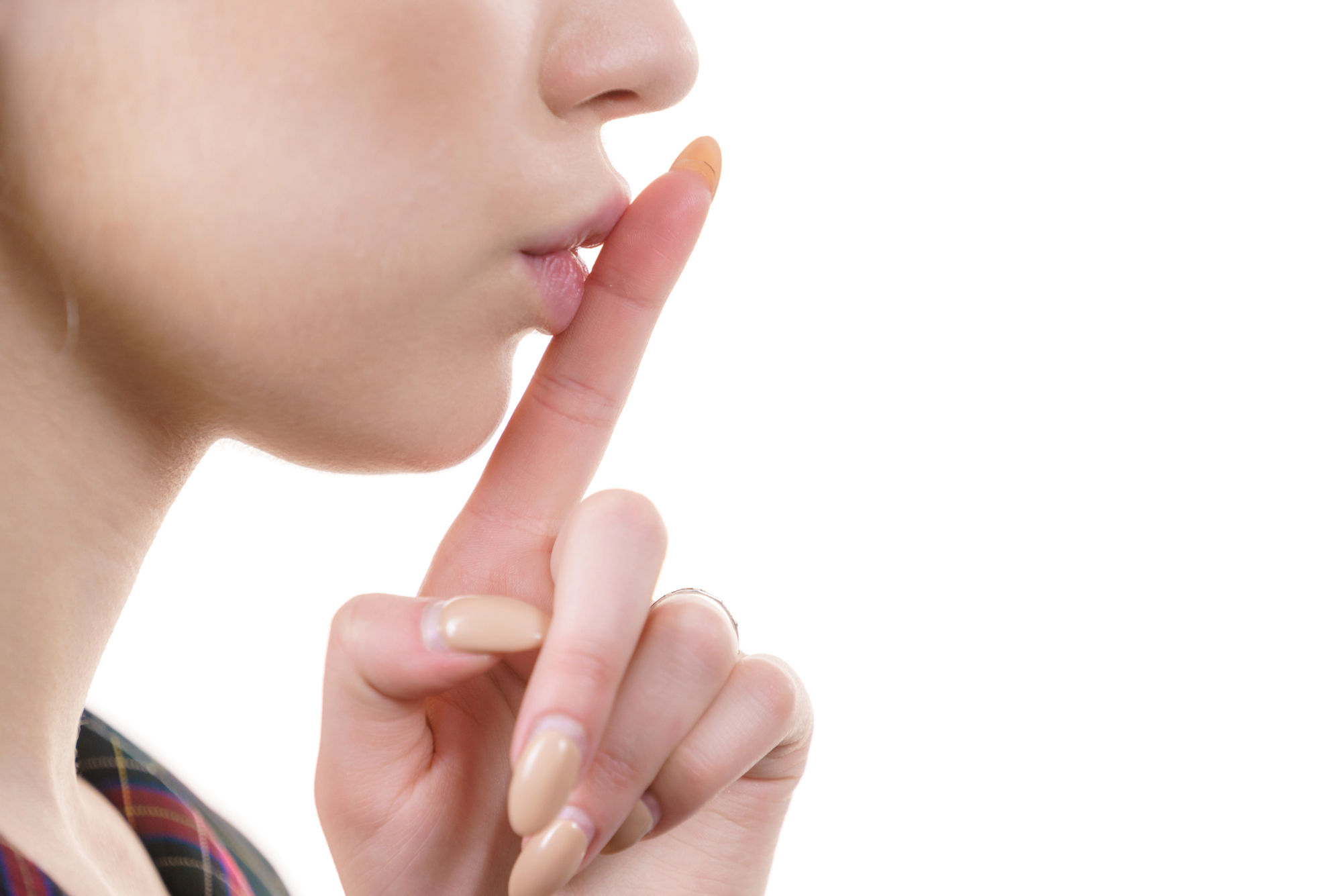 Close-up of a person's face, shown in profile, with their index finger pressed to their lips in a "shhh" gesture. The background is white, and the person has light skin, wearing natural-toned nail polish with long nails.