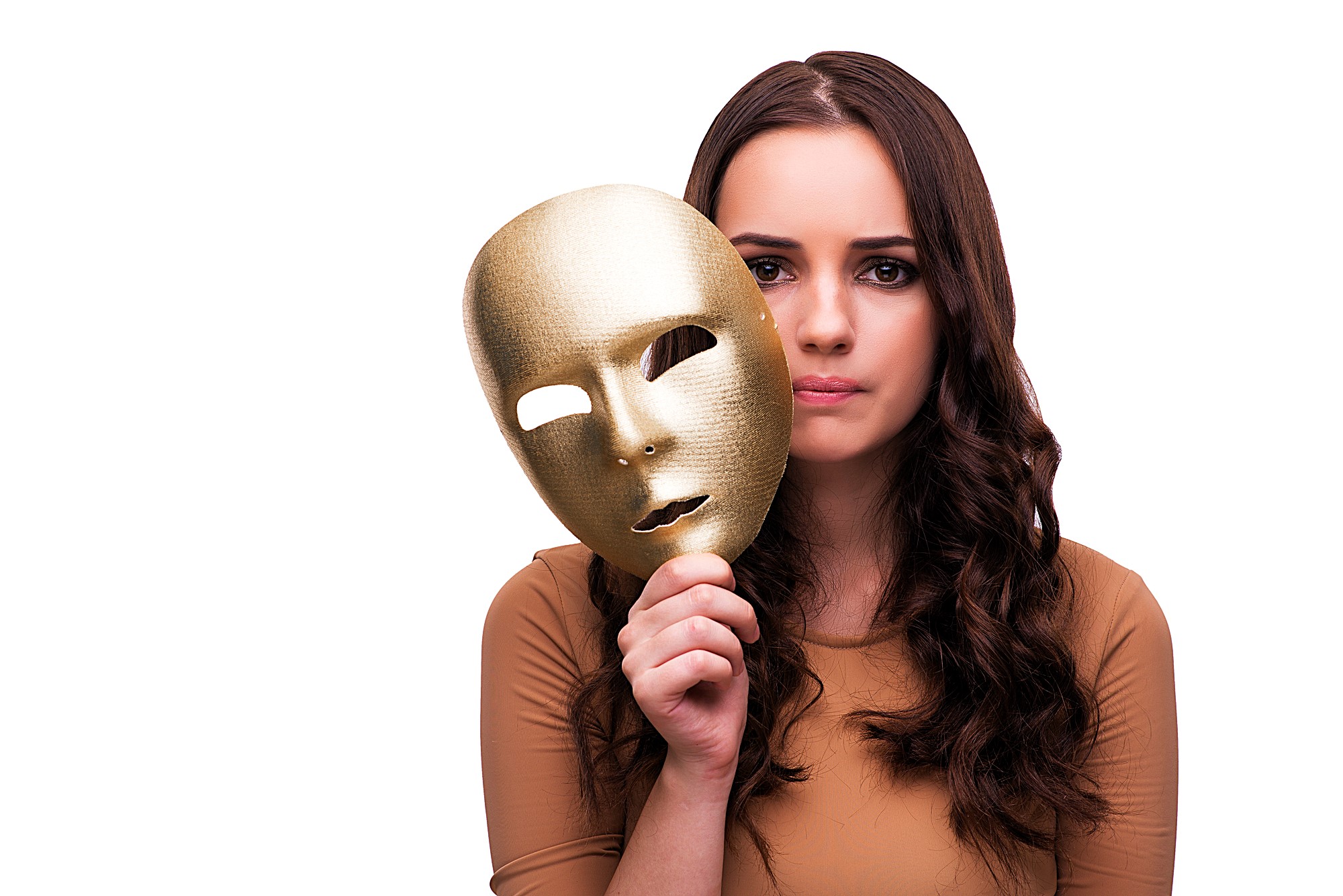 A woman with long, wavy brown hair holds a gold mask with empty eye holes in front of her face. She gazes at the camera with a neutral expression. She is wearing a beige top and has the mask positioned to the side of her face, revealing her features.