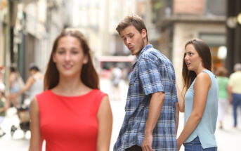 A young man in a blue plaid shirt looks at a woman in a red dress walking by, while another woman in a blue top, presumably his partner, stands next to him looking surprised and unhappy. The scene takes place on a busy, sunlit street.