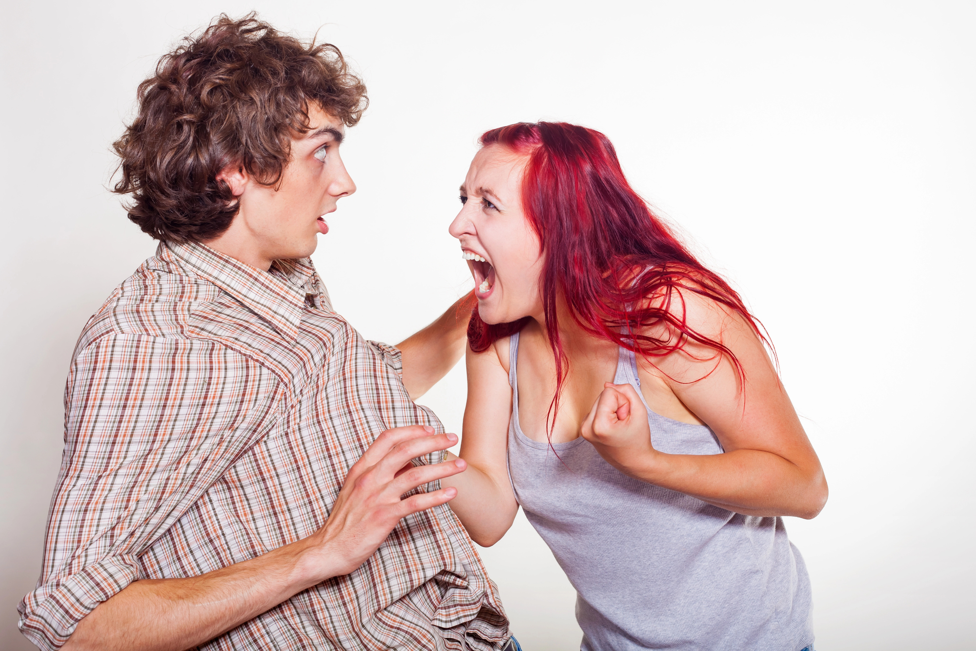 A young woman with red hair is shouting at a young man with curly brown hair. The man appears startled, pulling back slightly with his hands raised defensively. The woman has a clenched fist, and both are against a plain white background.