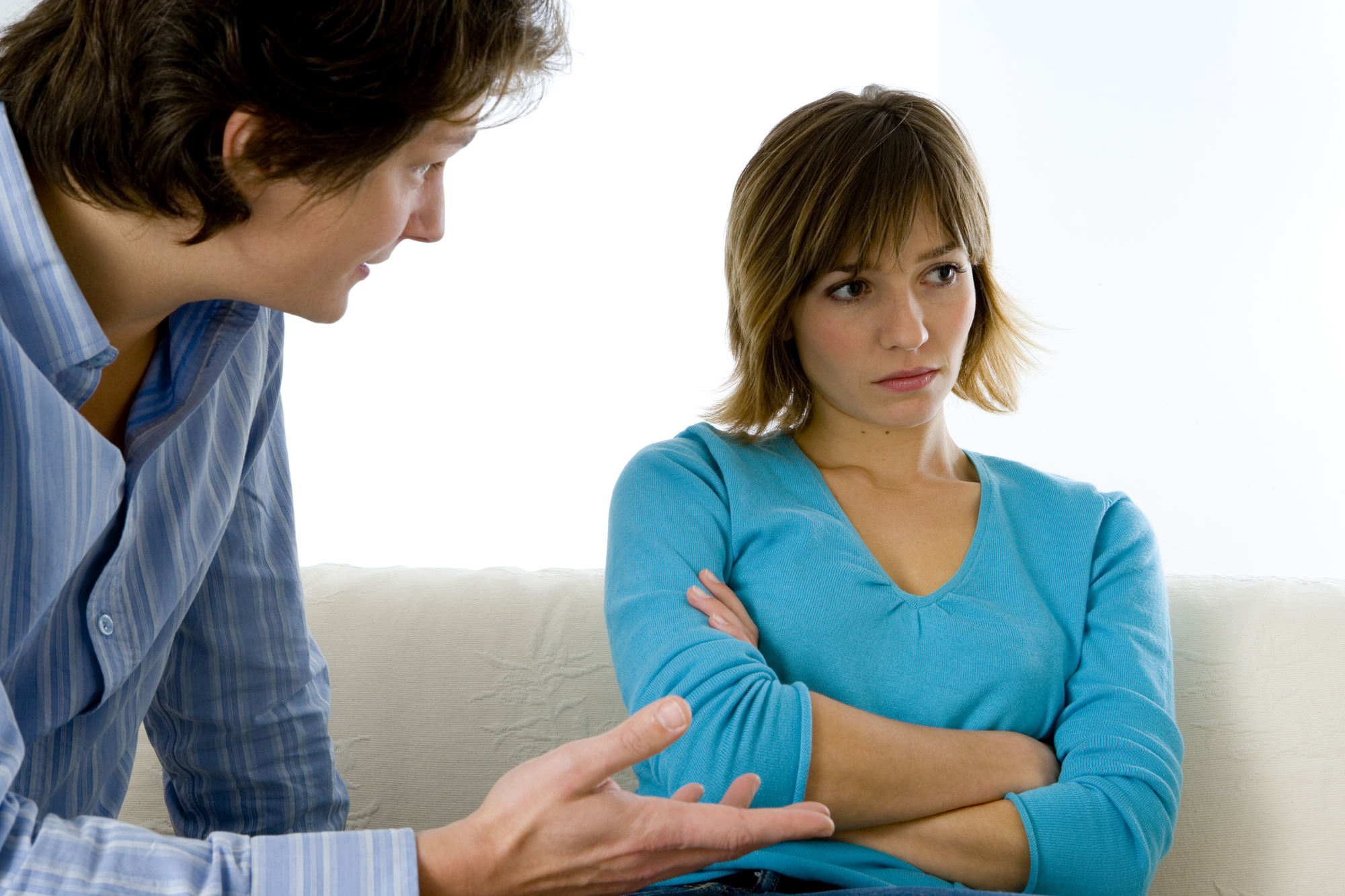 A person with short hair and a blue sweater is sitting with their arms crossed, looking away. Another person with medium-length hair and a striped shirt is standing nearby, gesturing with one hand, appearing to be in a serious conversation.