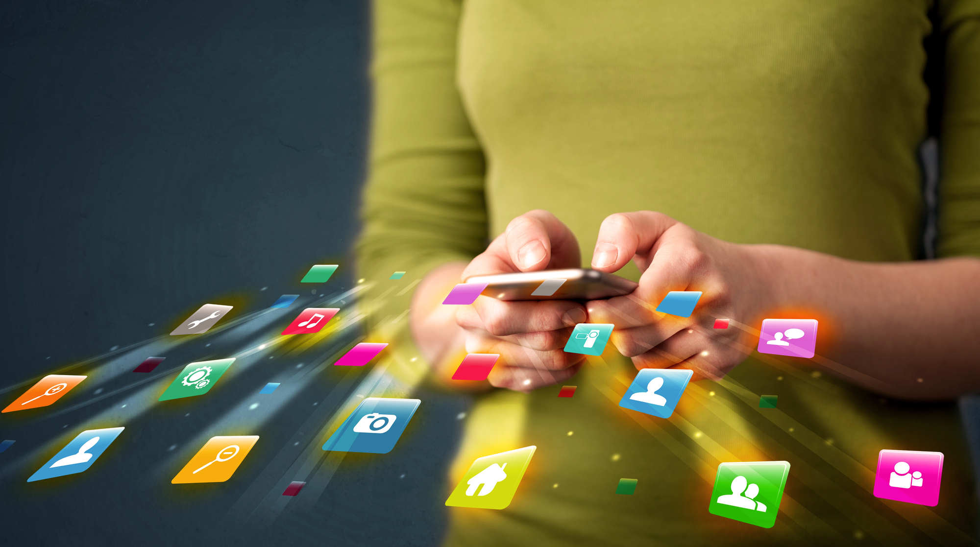 A person wearing a green shirt uses a smartphone. Colorful application icons, including camera, house, chat, and settings, are floating in the air around the phone, representing various digital apps and services. The background is dark and blurred.