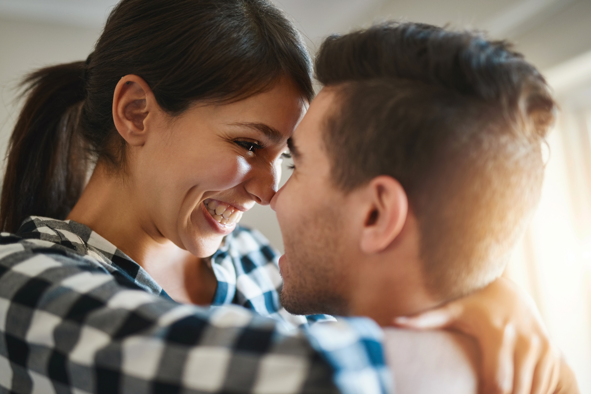 A woman and a man are embracing each other joyfully. The woman is smiling widely, and they are looking into each other's eyes, conveying a sense of happiness and affection. She has her arms around his shoulders, and he is holding her close.