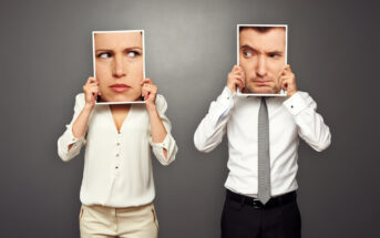 Two people standing against a gray background hold photos of faces over their own. The person on the left has a skeptical female face, while the person on the right holds a suspicious male face. Both wear formal white tops.