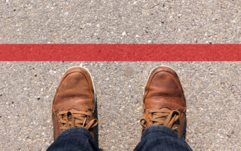 Person wearing brown leather shoes standing on a concrete surface just behind a red line, suggesting a boundary or finish line.