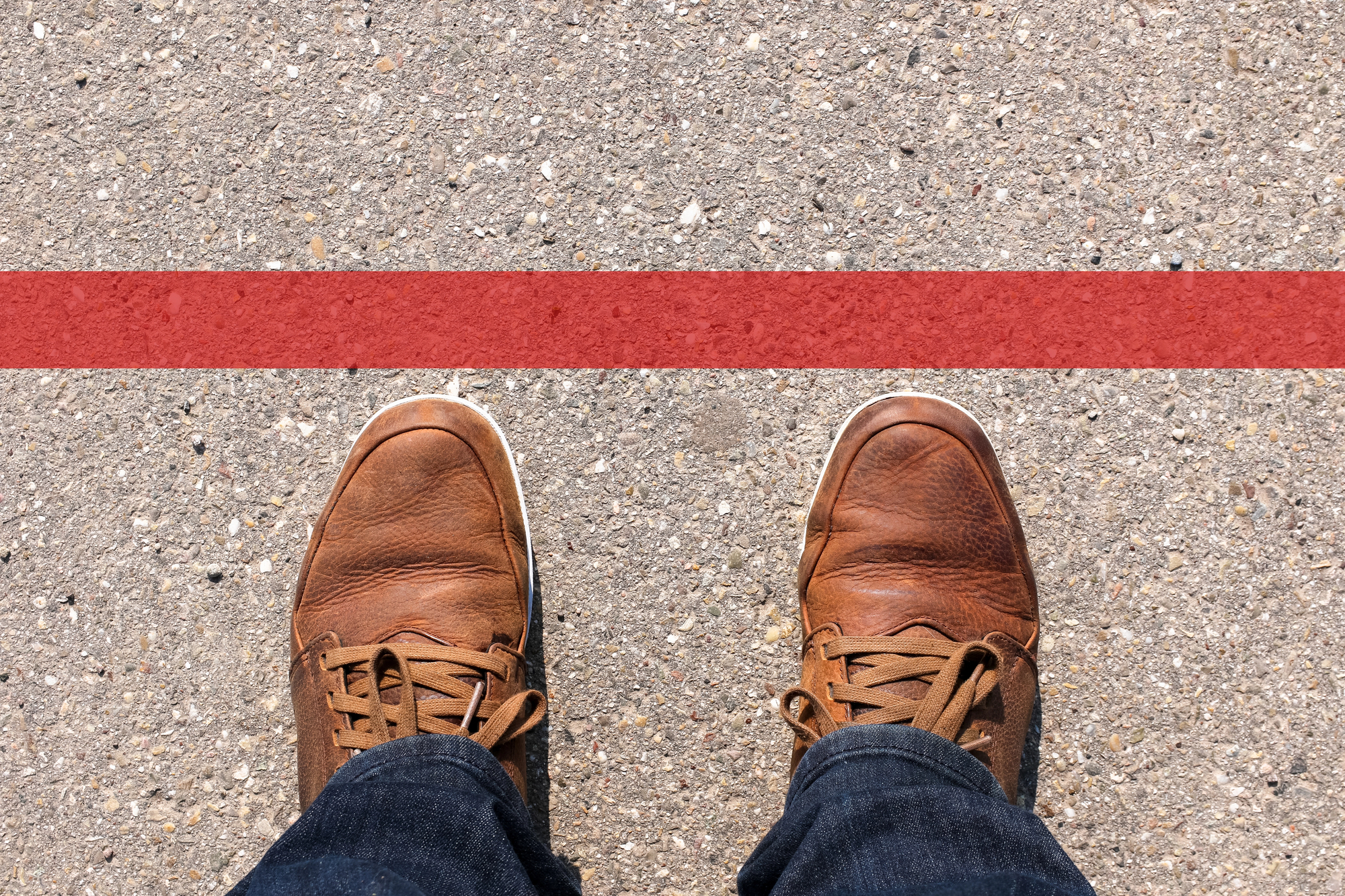 Person wearing brown leather shoes standing on a concrete surface just behind a red line, suggesting a boundary or finish line.