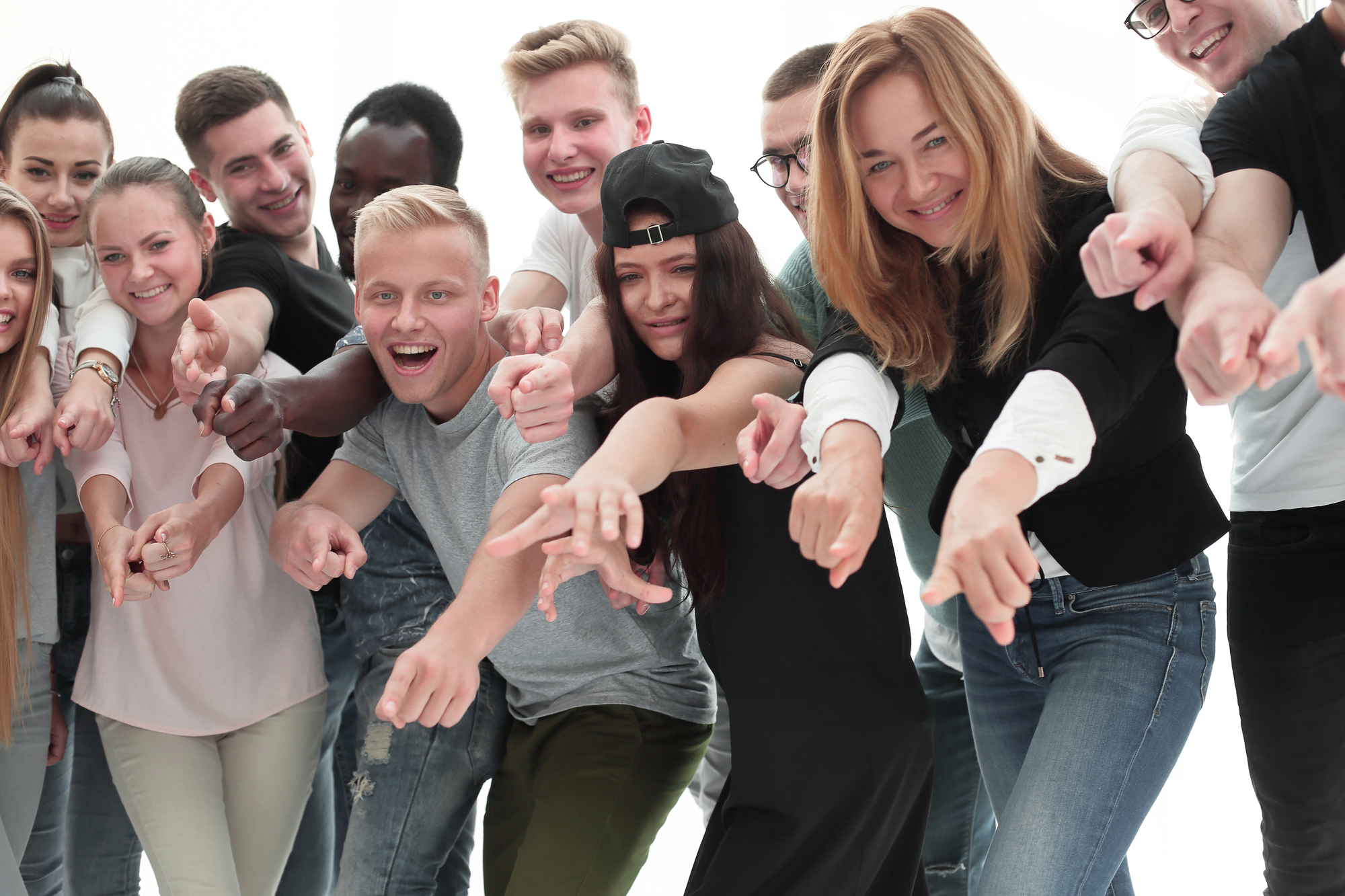 A diverse group of young people smiling and pointing towards the camera, standing close together. They appear cheerful and energetic. The background is bright and white.