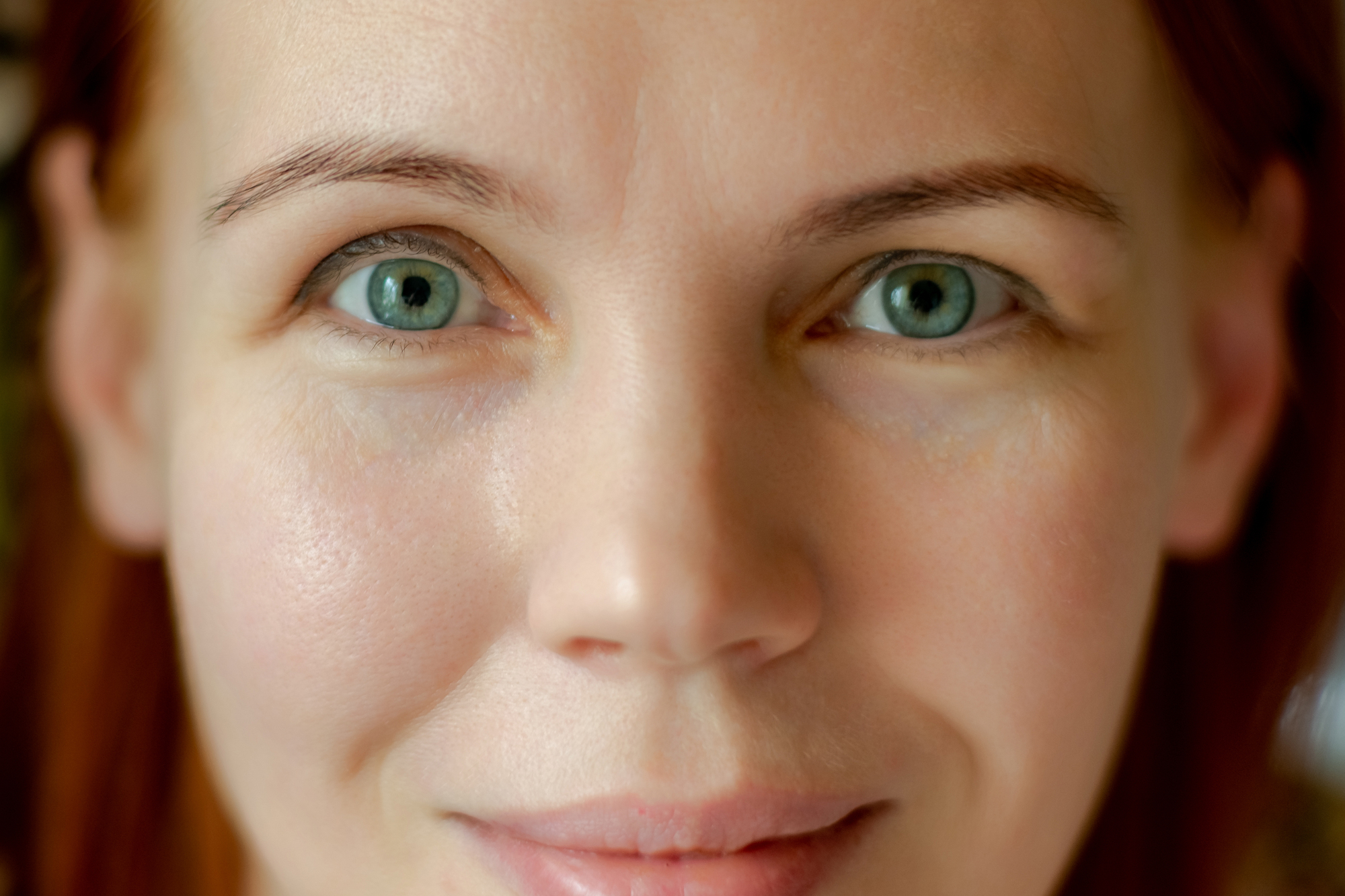 A close-up of a person with light skin and green eyes, softly smiling. The background is out of focus.