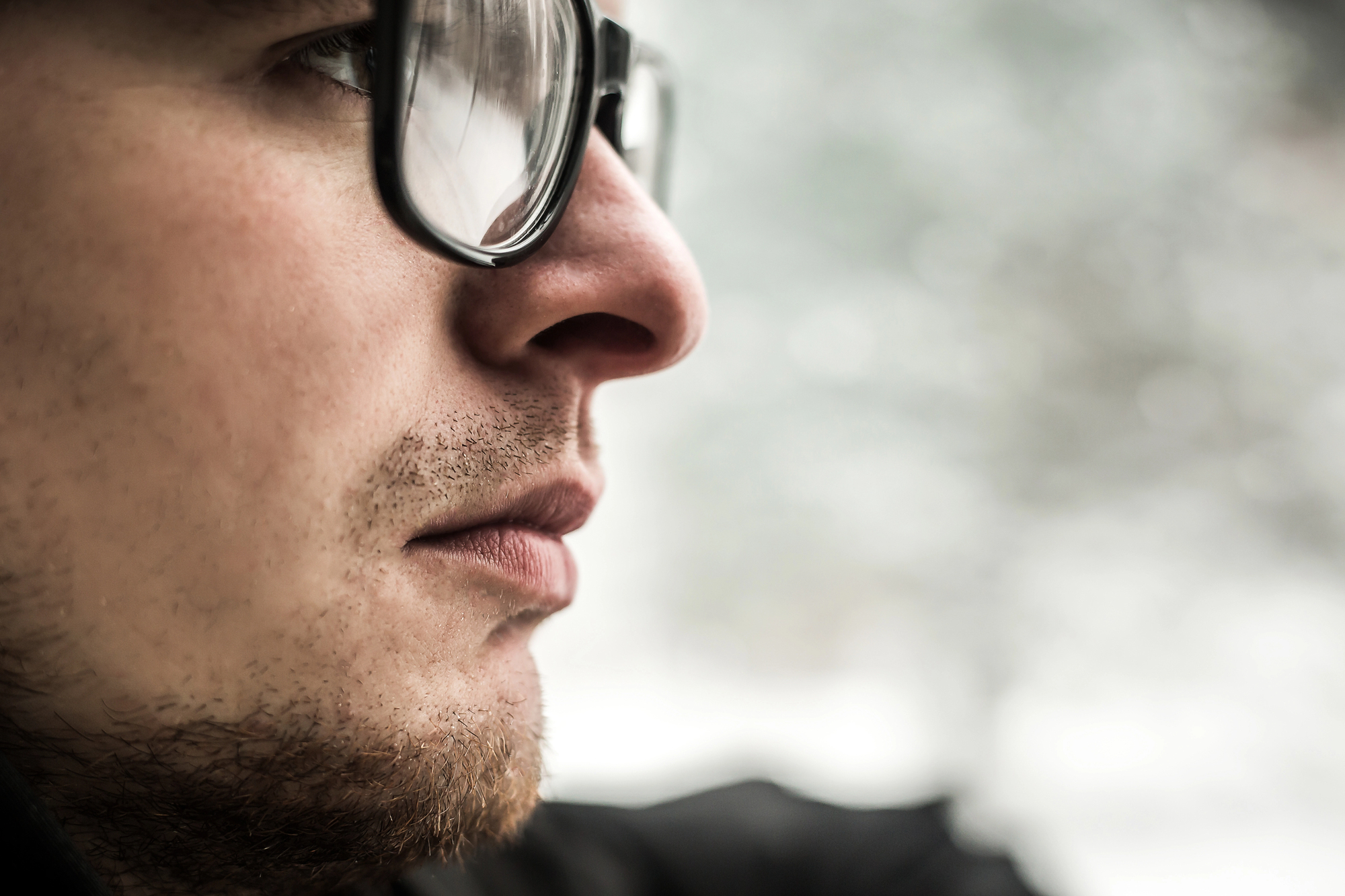 A close-up side profile of a person wearing glasses, with a focused expression. The background is blurred, suggesting an outdoor, possibly snowy setting. The image emphasizes facial details and glasses.