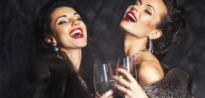 Two women, dressed in elegant fur coats and sparkling jewelry, are laughing and raising glasses of champagne. Their hairstyles and makeup are glamorous, and they are set against a dark, textured background.