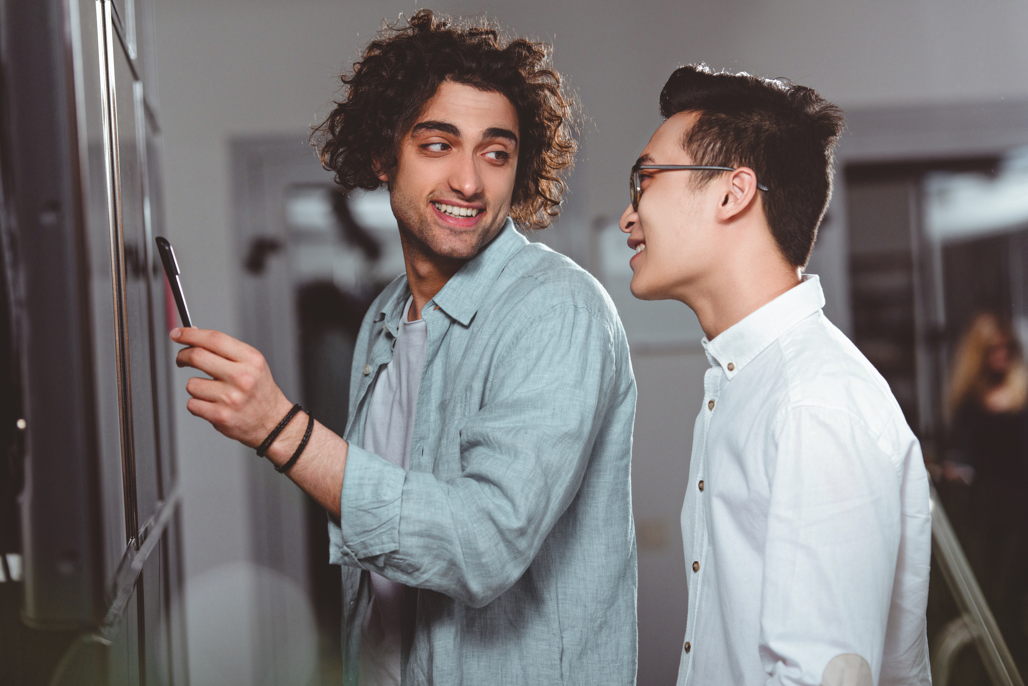 Two people are smiling and discussing something on a screen. One is pointing with a stylus, and both are dressed casually. They seem engaged and happy in a modern office environment.