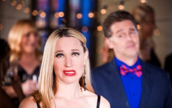 A woman with long blonde hair makes an awkward expression while standing at a party, adorned with string lights. A man in a blue shirt and patterned bow tie stands behind her, appearing unfocused and slightly perplexed. Other guests are blurred in the background.