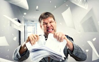 A man in a suit angrily tearing apart a stack of papers in a hallway. Papers are flying around him, creating a chaotic scene. His facial expression shows frustration and intensity. The hallway is brightly lit.