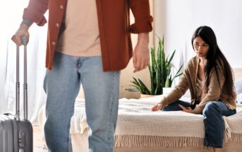 A woman sits on a bed looking upset, while a person in jeans and a brown shirt walks away holding a suitcase. There is a plant next to the bed, and the room has a soft, neutral color palette.