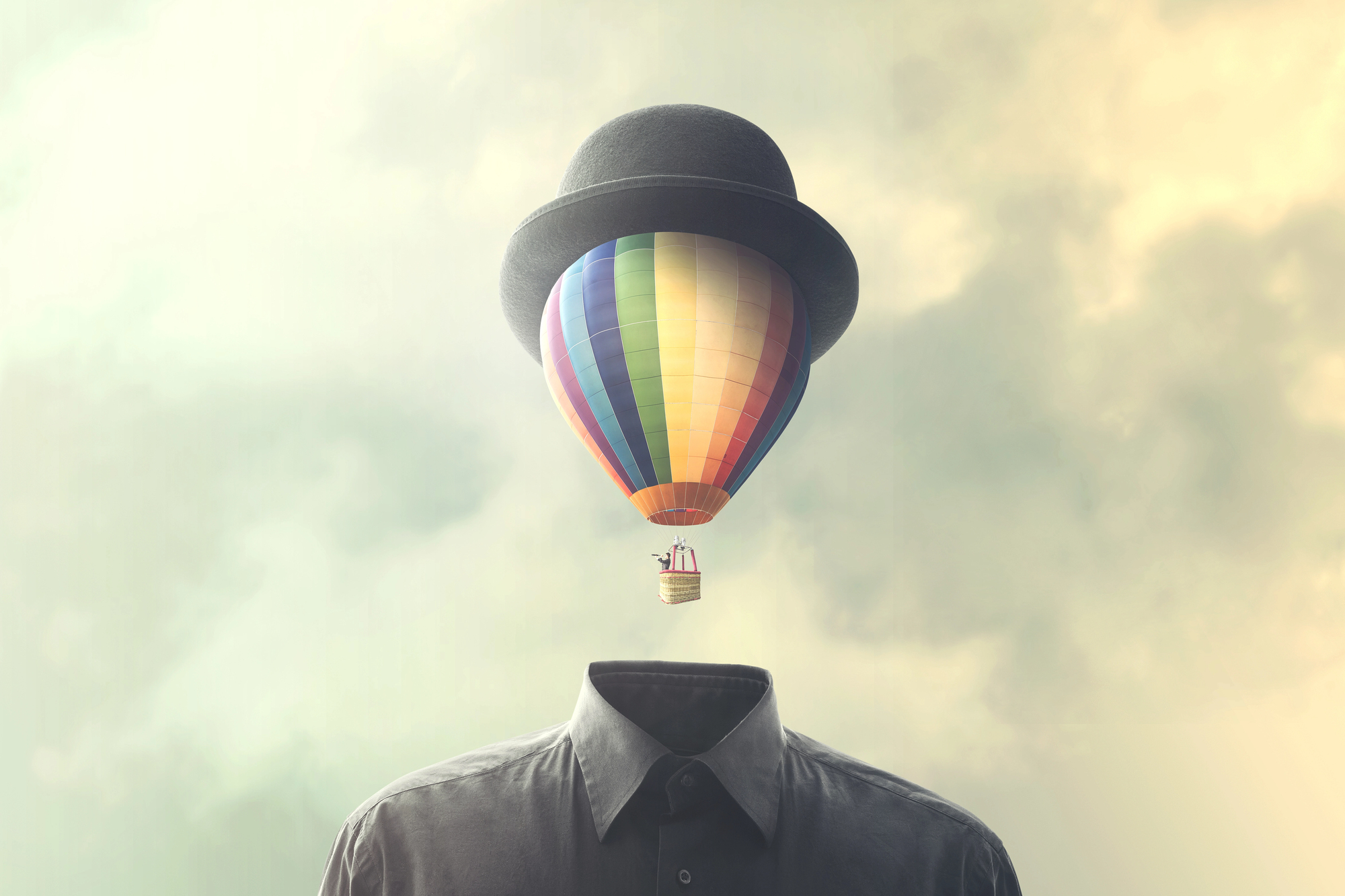 A surreal image of a hot air balloon with a rainbow-colored balloon and a basket, topped with a black bowler hat. The balloon is positioned above a headless shirt against a cloudy sky, creating an imaginative scene.