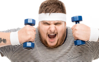 A person wearing a striped shirt, a white headband, and wristbands is energetically lifting two small blue dumbbells against a white background. They have an intense expression, showcasing determination and effort.